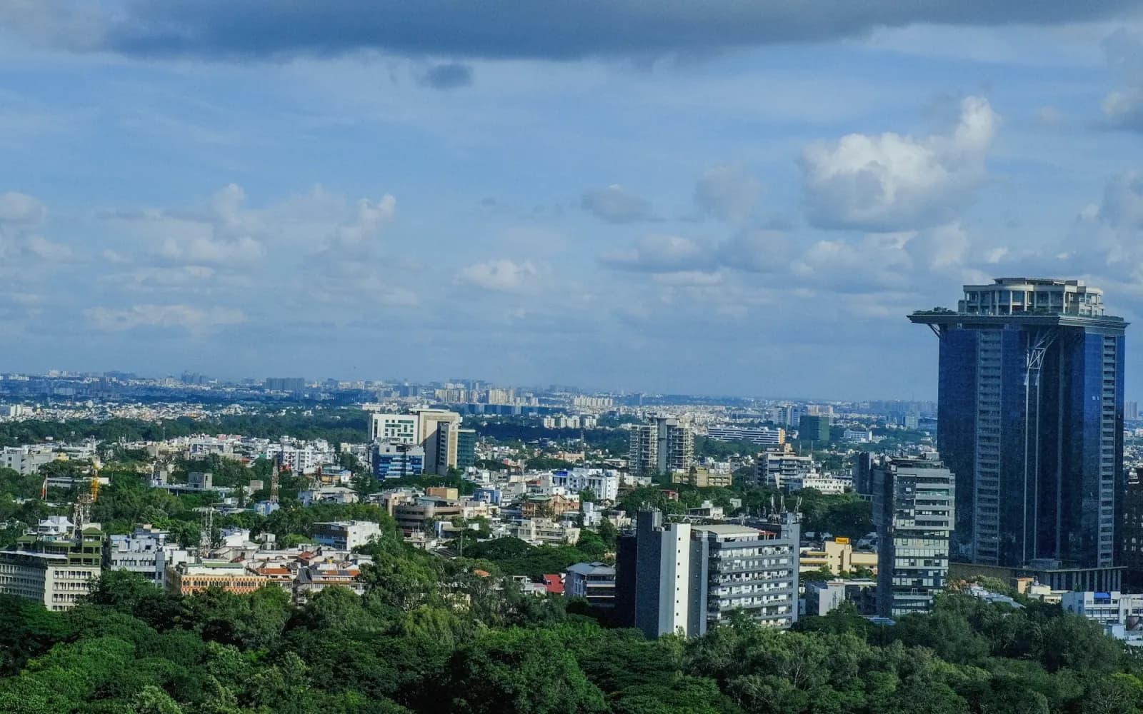 Bangalore skyline with Kingfisher Towers rising above tree cover and low-rise neighbourhoods under a bright sky